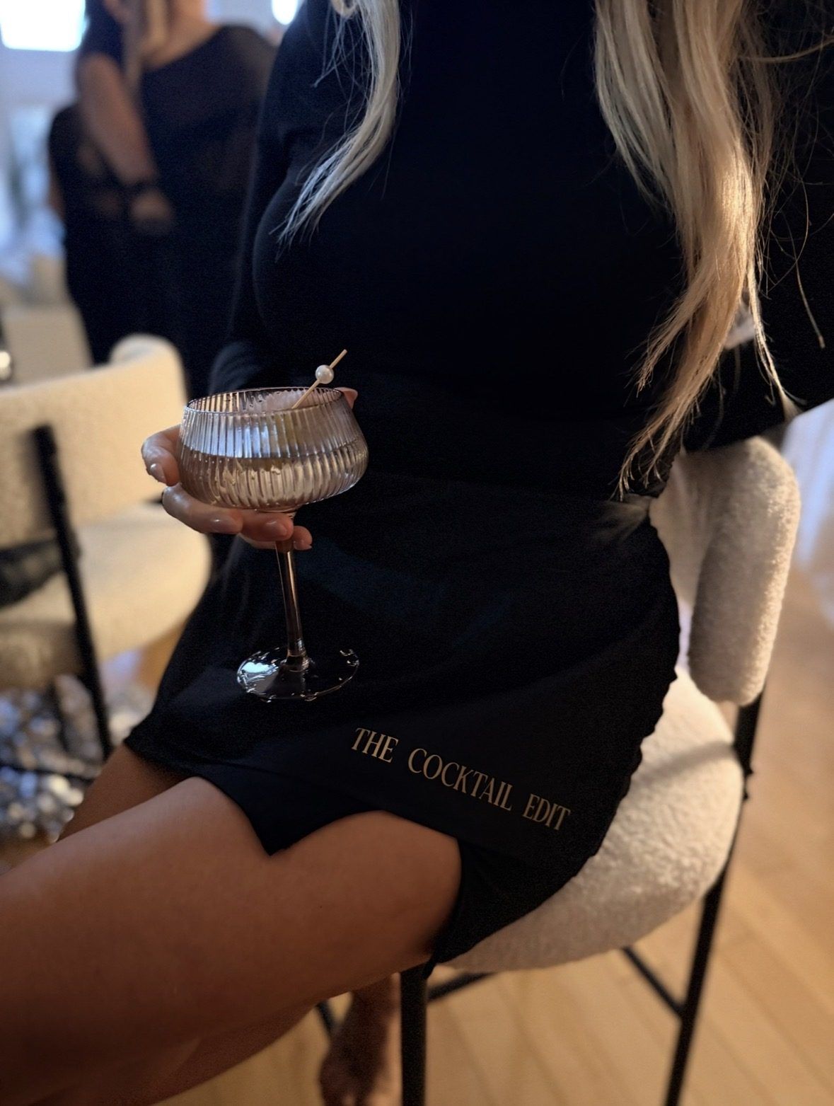 A guest holding a coupe, wearing a The Cocktail Edit apron